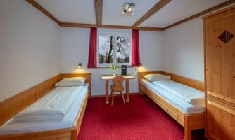A cozy room with two single beds and a small table. Red curtains and wood paneling create a pleasant atmosphere.