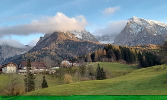 A picturesque landscape with mountains and green meadows. In the foreground, some houses and trees are visible.