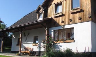 A charming house with wooden cladding and a well-maintained garden. The entrance area is welcoming with plants and a seating area.