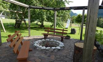 A cozy spot with a fire pit and wooden benches. The surroundings are lush and inviting.