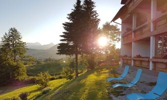 A picturesque garden with a view of the mountains and sunset. Relaxing loungers are placed next to a beautiful building.