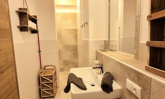 A modern bathroom with a bright, minimalist design. There is a sink, a shower, and wooden details in the decor.