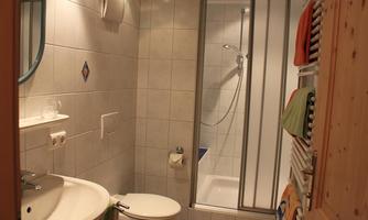A modern bathroom with tiles, a sink, and a shower cubicle. Colorful towels hang on a towel warmer.