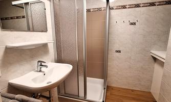 A modern bathroom with a shower, sink, and wooden floor. The walls are beautifully tiled in light colors and well-lit.
