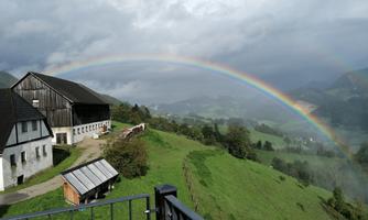 A picturesque landscape with green meadows and a farmhouse. A colorful rainbow stretches across the sky.