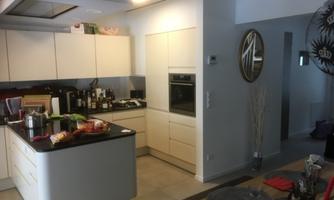 A modern kitchen with white cabinets and a black workspace. The room is bright and tidy, with various utensils and food items on the countertop.