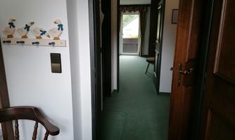 A bright corridor with green carpet and open doors to other rooms. Decorative elements hang on the wall.