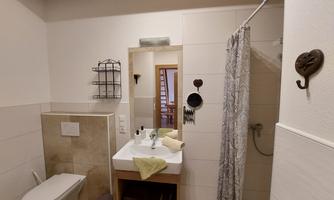 A modern bathroom with a shower, a sink, and a toilet. The walls are bright and the furnishings are minimalist.