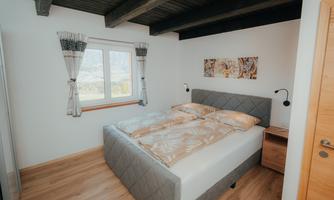 A cozy bedroom with a double bed and modern nightstands. Plenty of light comes in through the window, and the walls are painted in neutral colors.