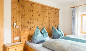A cozy bedroom with wooden paneling and modern cushions. The window lets in plenty of light and creates a bright atmosphere.