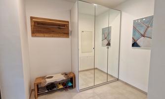 An inviting hallway with a large mirror and a wooden bench. Decorative pictures hang on the wall, and the floor is brightly tiled.