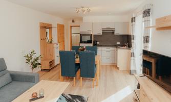 A bright and modern living room with a cozy couch and a dining table. The open kitchen is well-equipped and offers a pleasant living area.