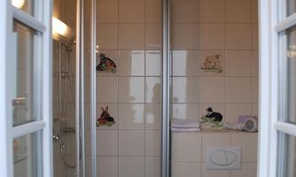A small bathroom with a shower and toilet. Bright tiles and a window create a friendly impression.