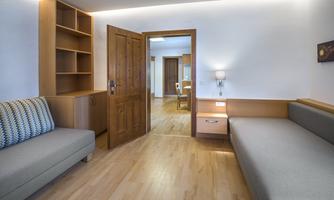 A bright, modern living space with wooden shelves and two sofas. The open door leads to another area of the room.
