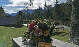 A beautiful bouquet of colorful flowers is on a table. In the background, trees and mountains can be seen under a clear sky.
