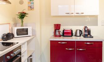 A modern kitchen with red cabinets and white surfaces. On the countertop are a microwave, a coffee machine, and a kettle.