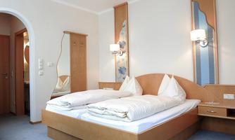 A modern bedroom with a double bed and two pillows. The walls are light and there is a large mirror as well as soft lighting.