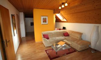 A cozy living room with a beige couch and decorative pillows. The room has wood paneling and a large window area that lets in plenty of light.