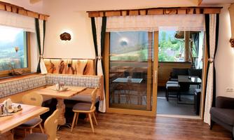 A cozy restaurant with wood colors and elegant tables. The large window front offers a view of the surrounding nature.