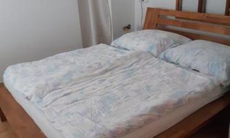 A cozy bedroom with a large wooden bed and two pillows. The walls are light, and the room feels welcoming.