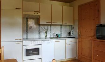 A modern kitchen with white cabinets and wooden details. On the countertop, there is a flower vase and various kitchen appliances.