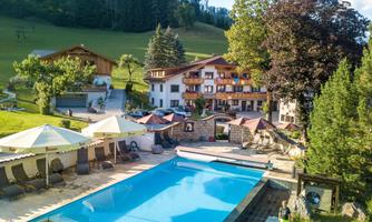 A picturesque hotel with an inviting pool and sun umbrellas. Surrounded by green hills and trees, it offers a relaxed atmosphere.
