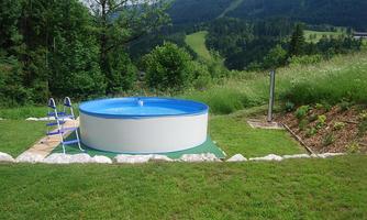 A round pool stands on a green meadow overlooking gentle hills. In the background, trees and a picturesque landscape can be seen.