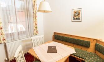 A cozy dining area with a wooden bench and table. Curtains with a floral pattern hang in front of the window.
