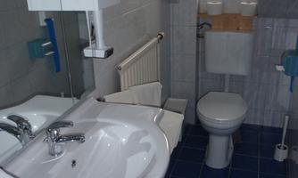 A simple bathroom with a white sink, a toilet, and blue tiles. There is a window that lets in daylight.