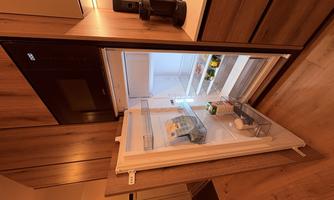 An open refrigerator in a modern kitchen. It contains some food items and is well-lit.
