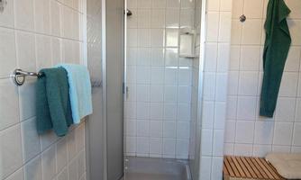 A modern bathroom with a glass shower. There are towels in various colors and a wooden bench for added functionality.