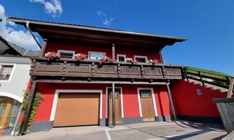 A red house with a wooden balcony and colorful flowers. The clear blue sky creates a friendly atmosphere.