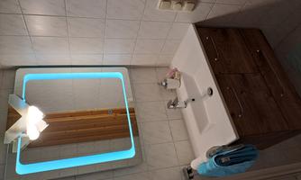 A modern bathroom with an elegant sink and a lit mirror. The walls are tiled, and there are towels and bathroom accessories.