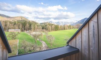 A beautiful view of green meadows and mountains under a clear sky. The landscape is calm and inviting.
