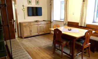 A cozy living area with a wooden table and four chairs. On the wall, there is a flat-screen TV and a wooden sideboard.