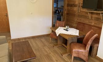 A cozy living space with a wooden table and two chairs. The walls are made of wood and there is a television on the wall.