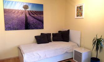 A cozy bedroom with a white bed and pillows. A picture of lavender fields under a blue sky hangs on the wall.