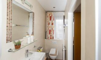 A modern bathroom with a sink, a large mirror, and a clear window view. The walls are bright and decorated with colorful curtains.