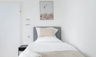 A simple, bright bedroom with a single bed and neutral colors. Two folded towels are on the bedspread.