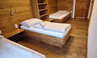 A simple room with three wooden single beds. The walls are also made of wood, and the floor is made of wooden parquet.