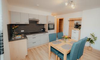 A modern kitchen with a dining table and chairs. The rooms are bright and friendly with wooden floors and clean lines.