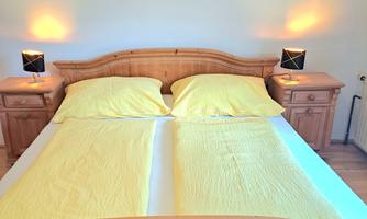 A cozy bedroom with a large wooden bed and yellow bedding. Two decorative pictures hang on the walls.