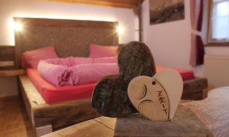 A cozy bedroom with a wooden bed and pink bedding. Two hearts made of stone and wood are decoratively placed on a table.