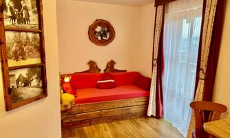 A cozy room with a red sofa and wooden elements. Bright curtains let in a lot of light.