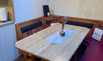 A cozy dining area with a large wooden table and red benches. A beautiful lamp hangs from the ceiling and provides warm light.