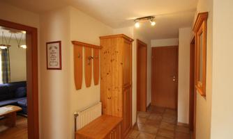 A bright hallway with wood interior and tiled floor. Coat hooks hang on the wall and there is an adjacent room with a sofa.
