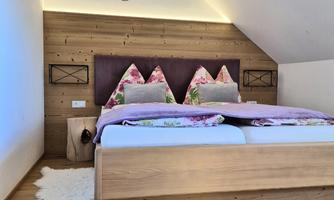 A cozy bedroom with a wooden bed and colorful pillows. The walls are wood-paneled and the decor is modern and inviting.