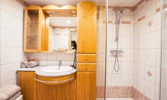 A modern bathroom with a round sink and wooden cabinets. The shower is clearly separated and the walls are tiled.
