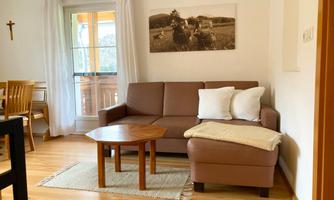 A cozy living room with a brown sofa, decorative cushions, and a wooden table. The light streams through the window, creating an inviting atmosphere.