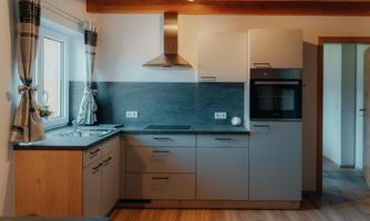 A modern kitchen with wooden ceiling beams and light furniture. The kitchen is well-equipped with a stove, an oven, and a sink.